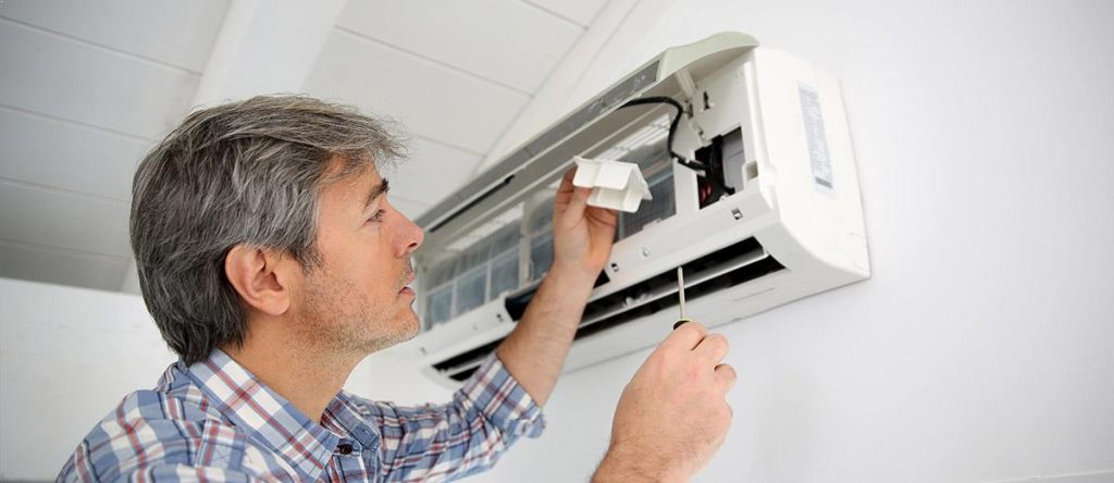 Air conditioner servicing benefits shown by technician cleaning wall mounted AC unit for better efficiency and air quality
